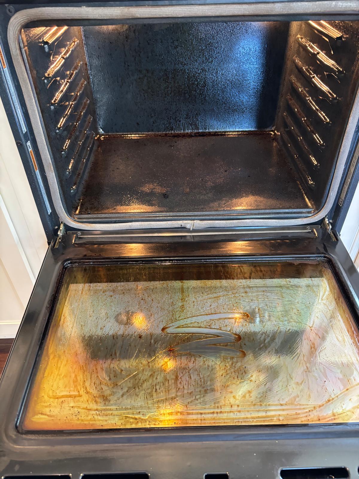 Open oven with grease on the interior and glass door before cleaning