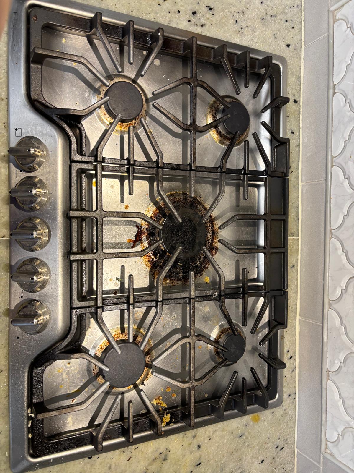 Stainless steel gas cooktop with grease and food spills before cleaning