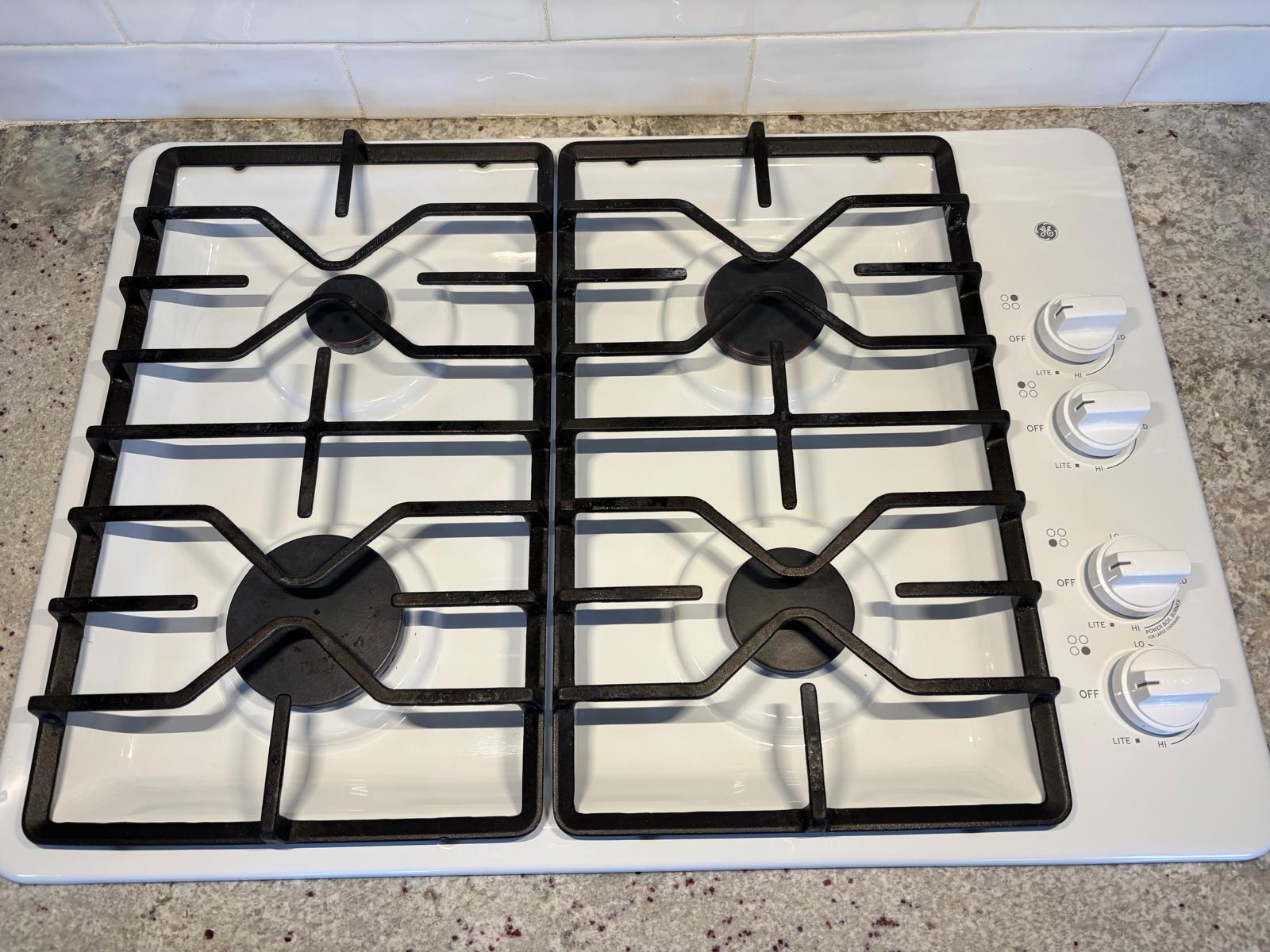 The same white gas cooktop after cleaning with grates and knobs in place