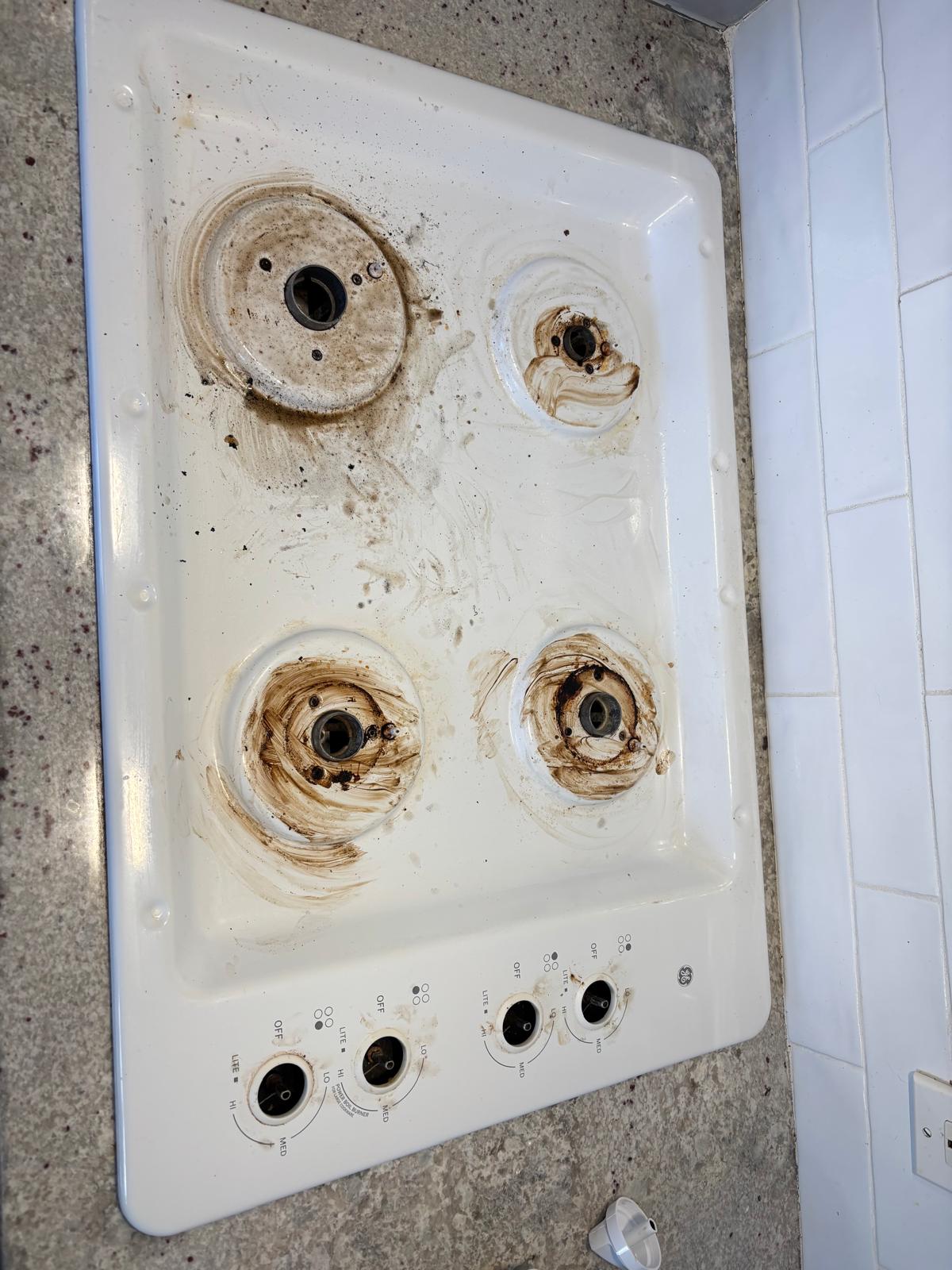 White gas cooktop with grease and food residue before cleaning